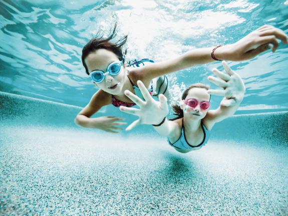Zwei Mädchen mit Schwimmbrillen unter Wasser im Schwimmbad